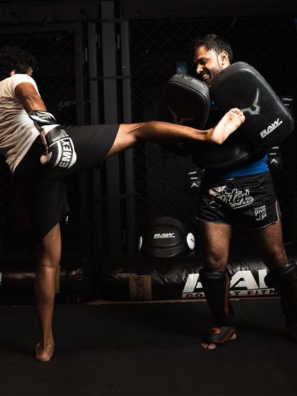 A fighter lands a clean side kick on the coach's body shield, demonstrating both power and accuracy.