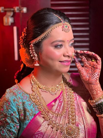 A candid moment of a bride on her wedding day. The traditional updo and matha patti frame her face beautifully, while the saree drape remains perfect.