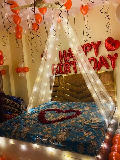A view focusing on the bed, adorned with a rose petal heart and framed by the glowing canopy and "Happy Birthday" balloons.