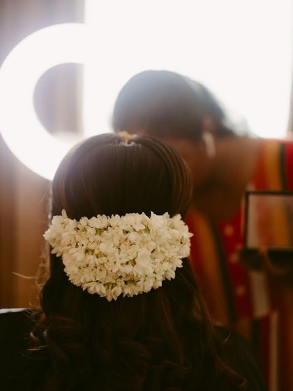A close-up of a bride's hair being styled with a traditional jasmine garland, with a ring light creating a beautiful halo effect.