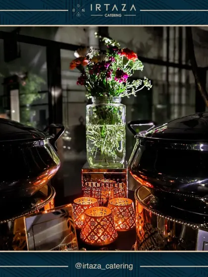 The interplay of light and decor is key to my setups. Here, fresh flowers in a simple glass vase are flanked by elegant copper and black chafing dishes, with the warm light from decorative candle holders creating a cozy and upscale feel.