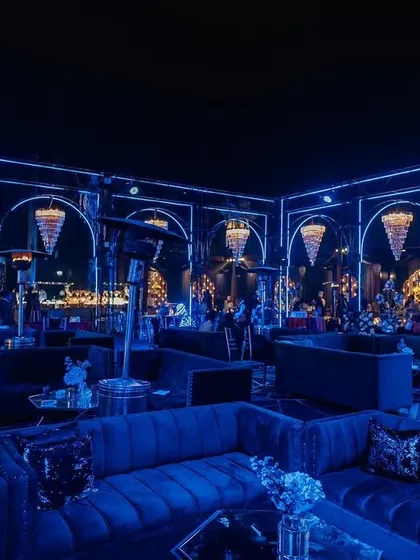 A stunning Sangeet setup with dramatic blue lighting and crystal chandeliers. The plush velvet seating and moody ambiance create a luxurious and glamorous party setting.
