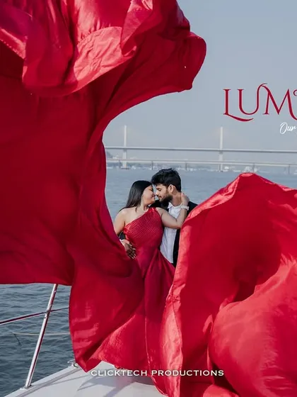 A dramatic, cinematic shot of a couple on a yacht in Goa, her vibrant red gown flowing in the wind, creating a powerful and luxurious image of a destination pre-wedding shoot.