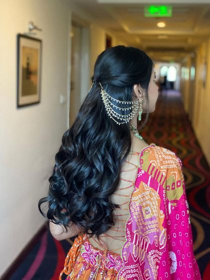 All set for her Mehendi with this classic half-up style. The soft curls and traditional kaan chain accessory create a timeless and elegant look.