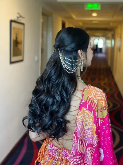 All set for her Mehendi with this classic half-up style. The soft curls and traditional kaan chain accessory create a timeless and elegant look.