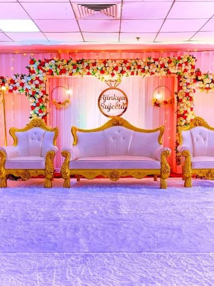 A full view of an engagement stage I designed. It includes a floral backdrop with custom signage for the couple, elegant lighting, and royal white and gold furniture for the seating area.