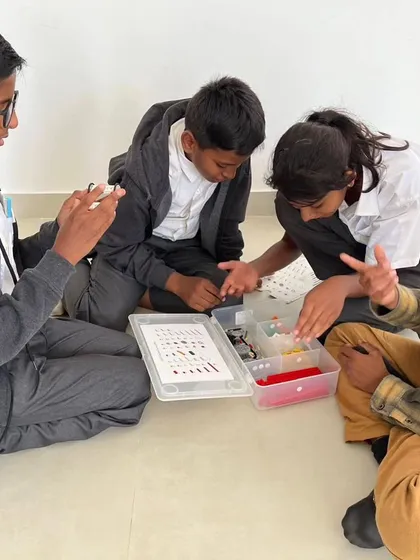 A group of students from Sadhu Vaswani International School discusses their strategy, pointing out different parts and planning their next move.