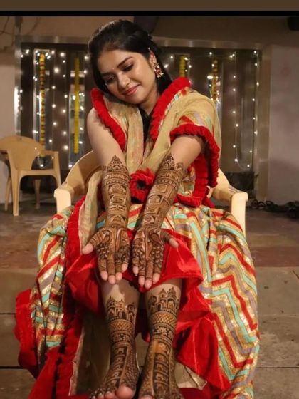 A candid photo of a bride admiring her full bridal mehendi, with both hands and feet beautifully decorated.