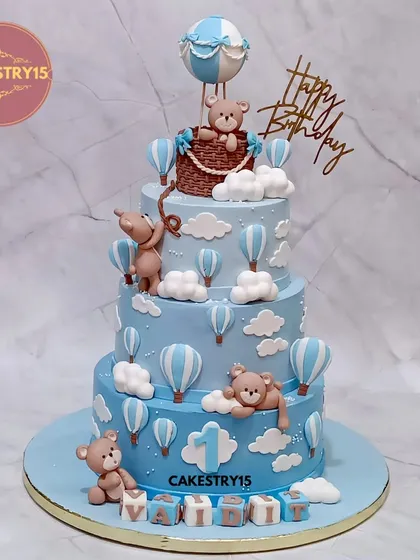 For a grand first birthday, we designed this three-tier chocolate cake with a whimsical hot air balloon theme. It features handcrafted fondant teddy bears, fluffy clouds, and a personalized name block, making it a delightful spectacle for a child's special day.