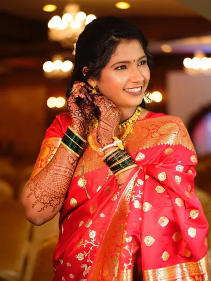 A happy bride putting on her earrings. Her makeup is fresh and glowing, and the red saree provides a beautiful, classic backdrop.
