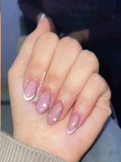 A simple and sweet design featuring a classic white French tip on some nails and tiny white hearts on a sheer pink base on others.
