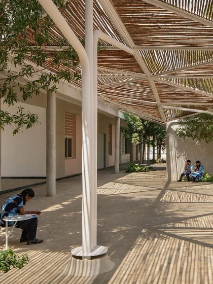 The undulating bamboo canopy connects the old and new school buildings, creating sheltered outdoor corridors and informal learning spaces where students can study or relax.