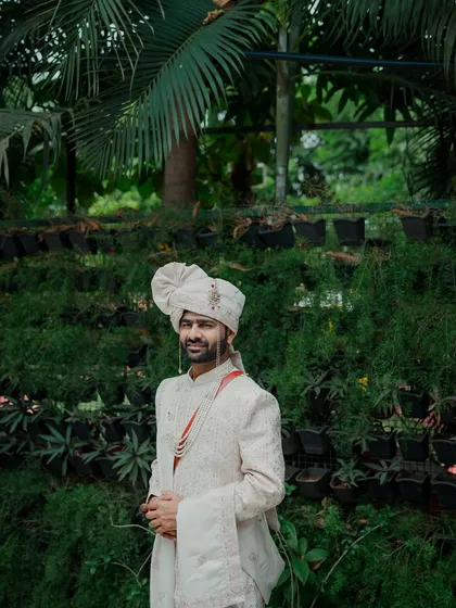 A full-length portrait of the groom standing confidently against a lush green background. His traditional attire and calm demeanor make for a very regal and handsome photograph.