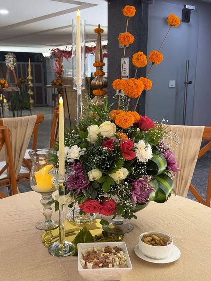 A centerpiece for the Lohri celebration, combining traditional orange marigolds with roses and other flowers in a modern arrangement. The tall candles add a touch of elegance to the table.
