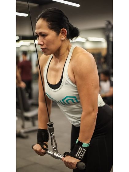 With intense focus, a member performs a tricep pushdown using the straight bar attachment on the cable machine.