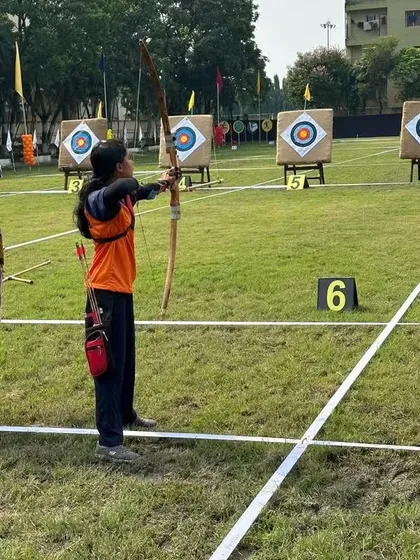 A young archer at full draw during the national competition in Kolkata. She is using a traditional Indian round bow, showcasing a fundamental style of archery.