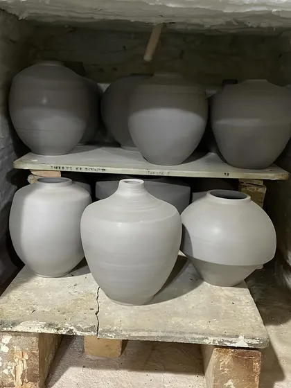 Unfired pots and Moon Jars drying on shelves in the kiln room. This slow drying process is crucial to prevent cracking during firing.