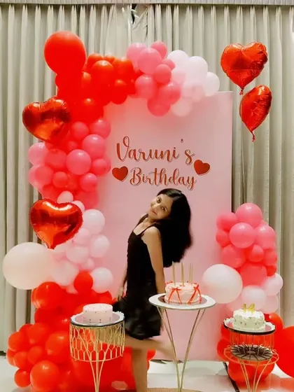 A lovely red and pink heart-themed birthday setup for Varuni, featuring heart-shaped foil balloons and a personalized backdrop.
