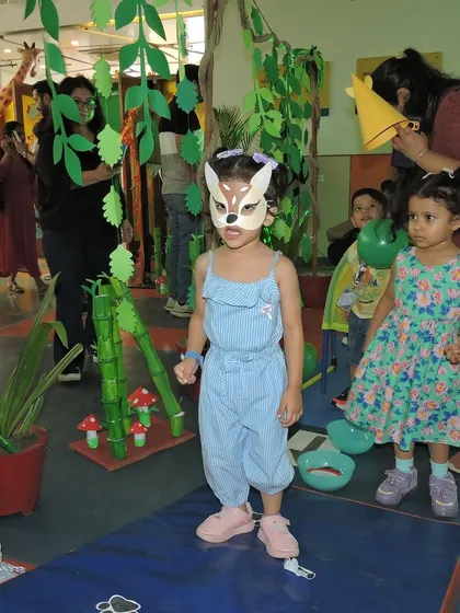 A young student dressed in a deer mask explores the 'Jungle Joyland' setup. We encourage imaginative play and participation from both children and parents at our community events.