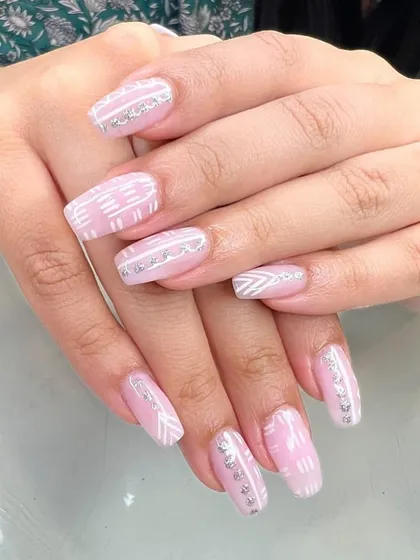 A beautiful pink manicure with intricate white line art and silver rhinestone accents.