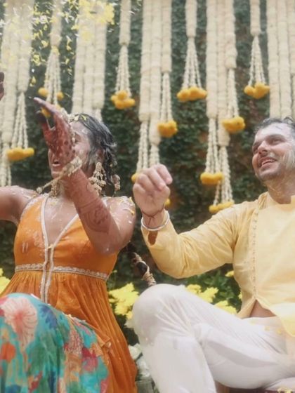 The couple sits together, drenched and smiling, during their outdoor Haldi ceremony, showcasing their joyful spirit.