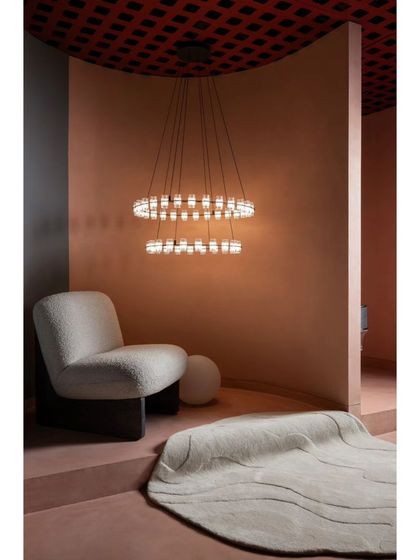 This cozy nook features a modern bouclé armchair and a tiered ring chandelier. We designed these spaces to feel like intimate living areas, helping customers visualize the lighting in their own homes.