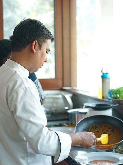 A chef plating a dish with care in a client's home. For large 'Easy Dining' orders, we send a chef to assist with heating, plating, and service.