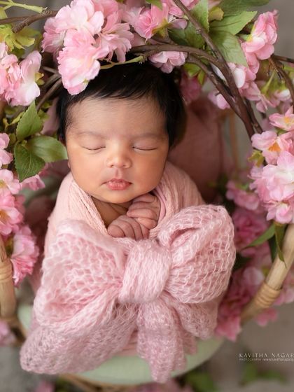 A newborn girl wrapped in a pink bow, nestled in a basket of cherry blossoms. This overhead shot creates a beautiful, floral-filled frame.