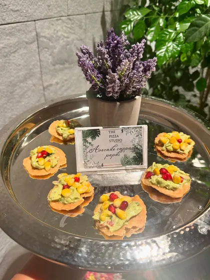 A creative take on a classic Indian snack. This is our avocado on papdi, topped with corn and pomegranate seeds, served on a silver tray. It's a perfect example of our Indian fusion offerings.