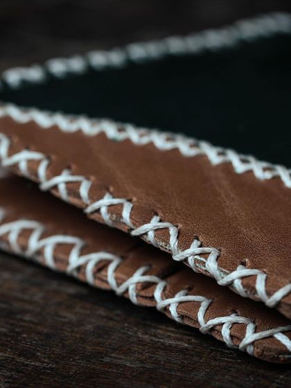 A duplicate of the detailed cross-stitching on a handmade leather wallet, highlighting the tactile quality of the craft.