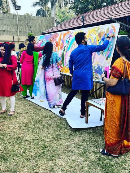 A wide shot of the group painting activity at an outdoor family event, with guests of all ages participating.