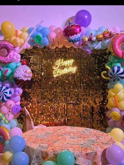 A candy-themed party with a gold sequin backdrop and a balloon arch featuring large donut and cupcake foil balloons.