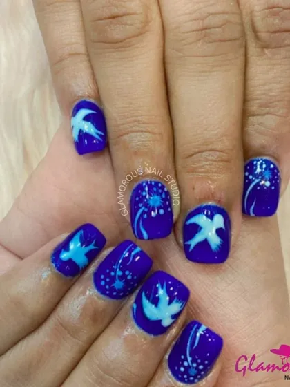 A whimsical design featuring deep blue nails with hand-painted dandelions and birds in flight, creating a dreamy, night-sky effect.