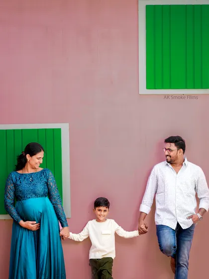 A fun and modern family portrait against a colorful studio wall. This shot captures the happy and relaxed dynamic of the family as they await their new addition.