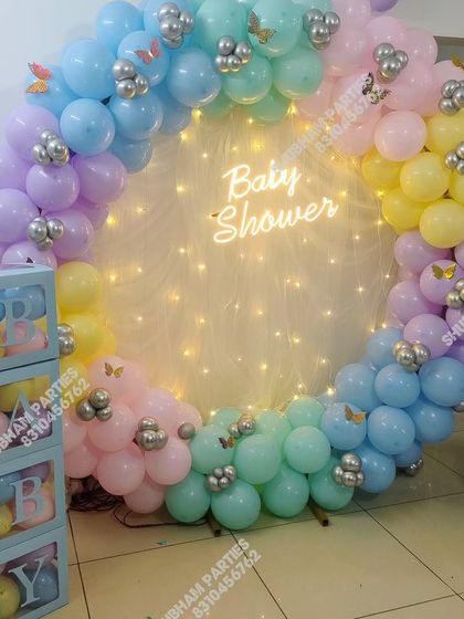 A pastel rainbow baby shower balloon ring with a neon sign and fairy lights.