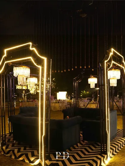 A modern, geometric lounge area for a Sangeet. The black metal frames with neon light outlines and chevron-patterned floor create a trendy, high-fashion vibe.