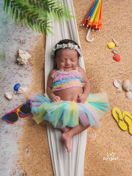 A day at the beach for our tiniest client. This creative flat-lay design uses sand, shells, and a mini umbrella to create a fun, sunny beach scene for this smiling newborn.