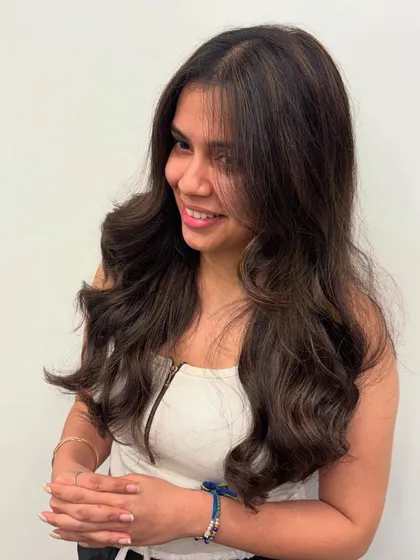 A happy client showing off her new hair color and style. The soft layers and waves complement the subtle balayage perfectly.