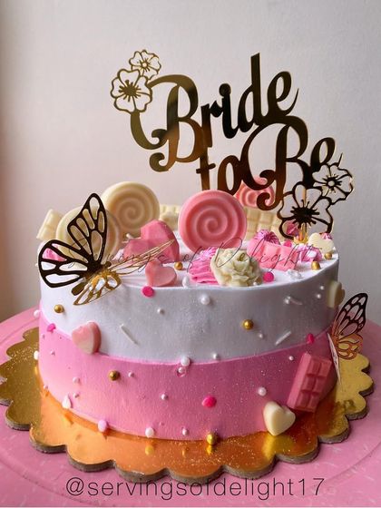 The prettiest "Bride to Be" cake in shades of pink and white. It's decorated with lollipops, butterflies, and chocolate hearts for a fun and girly celebration.