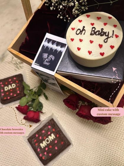 A closer look at the pregnancy announcement hamper. It includes a mini "Oh Baby!" cake, "Mom" and "Dad" brownies, and the couple's sonogram, all beautifully arranged to share the happy news.