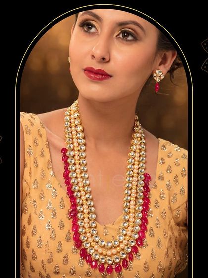 An ethnic Kundan long necklace set featuring three strands of Kundan and pearls, finished with beautiful ruby-red beads. It's a perfect piece for adding color and drama.