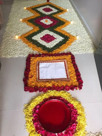 We specialize in detailed floral floor art, known as rangoli. This piece features intricate geometric patterns created with fresh petals of marigold, rose, and jasmine, with small diyas placed to add a warm glow.