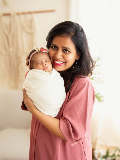 A proud mother smiling for the camera while holding her sleeping, swaddled baby. A beautiful portrait of motherhood.