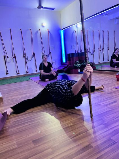 A student uses a stick prop to deepen a side split, working on hamstring and hip flexibility.