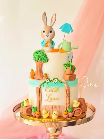 I brought the world of Peter Rabbit to life with this two-tiered buttercream cake. It features a hand-sculpted Peter Rabbit figure, a garden scene with tiny carrots and ducklings, and a personalized nameplate, making it a magical centerpiece for a first birthday.