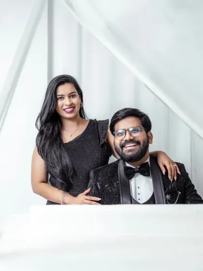 A high-fashion studio pre-wedding portrait. The couple is dressed in elegant black tie attire, and the falling feathers add a touch of magic and sophistication to this classic shot.