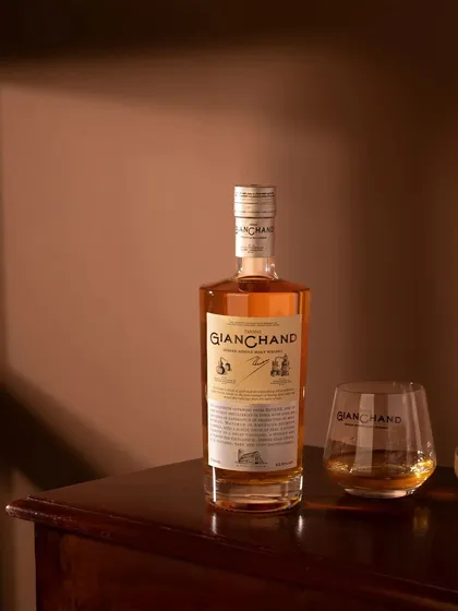 A lifestyle shot of Gianchand whiskey on a wooden table, using warm, soft light. This styling creates an inviting and relaxed atmosphere, showing the product in a natural home environment.