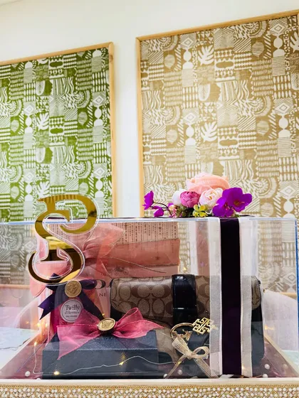 This wide shot shows another version of our acrylic trousseau box, filled with luxury accessories like a Coach pouch. The floral arrangement on top adds a soft, feminine touch.