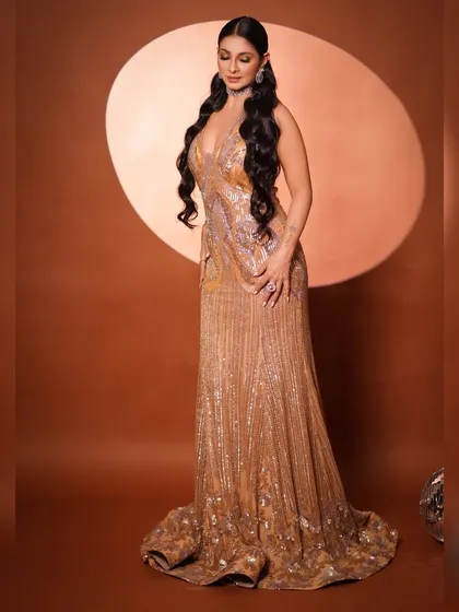 A full-length view of the magnificent gold sequined gown. The mermaid cut and the long, flowing hair create a dramatic and statuesque silhouette, perfect for a red carpet event.