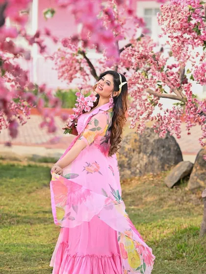 A full-length shot from a calendar shoot, with the model in a flowing pink dress against a backdrop of cherry blossoms. The image is vibrant, joyful, and full of life.